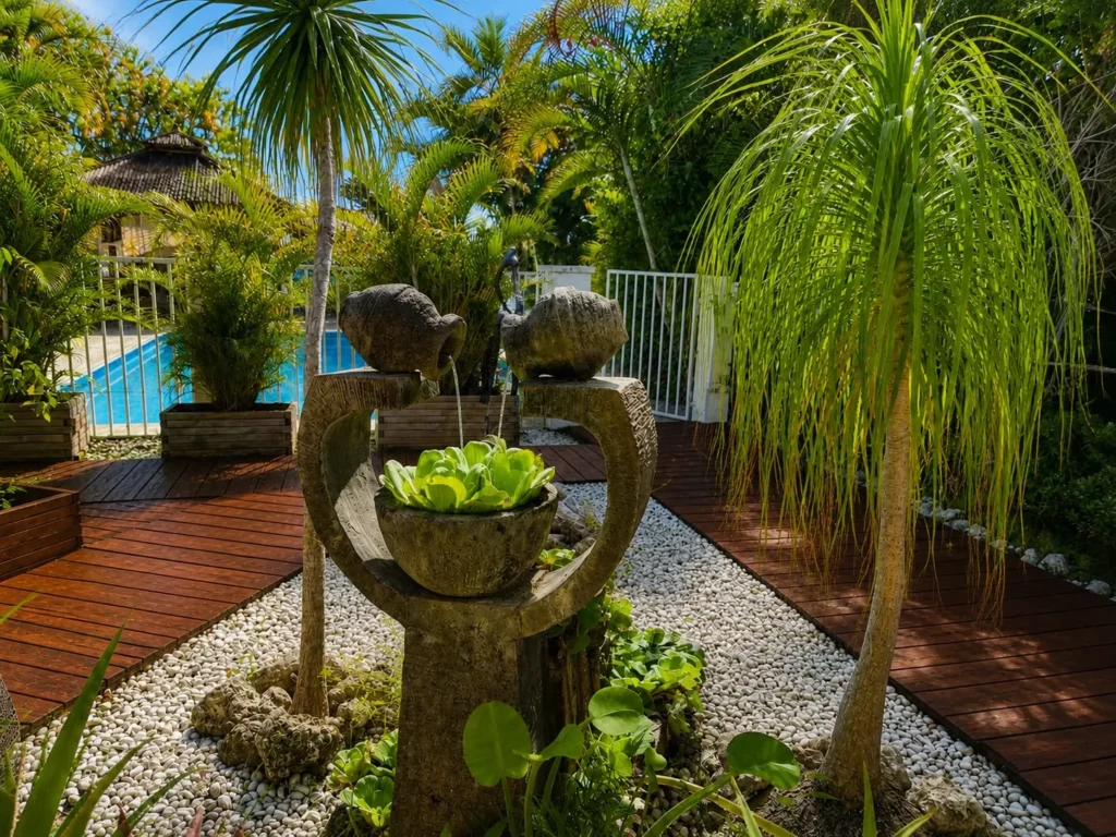 Fontaine en pierre sculptée entourée de végétation tropicale près de la piscine, dans le jardin du gîte Bois Banane aux Bois d'Orée, Sainte-Anne