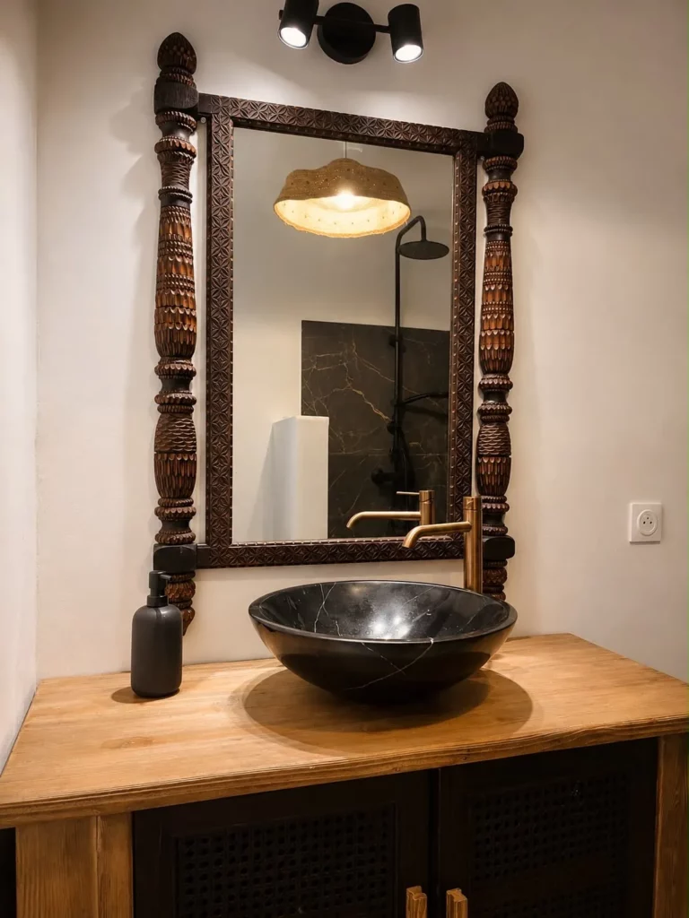 Salle de bain élégante avec vasque en pierre noire, miroir en bois sculpté et robinetterie dorée, gîte Bois Banane, Les Bois d'Orée
