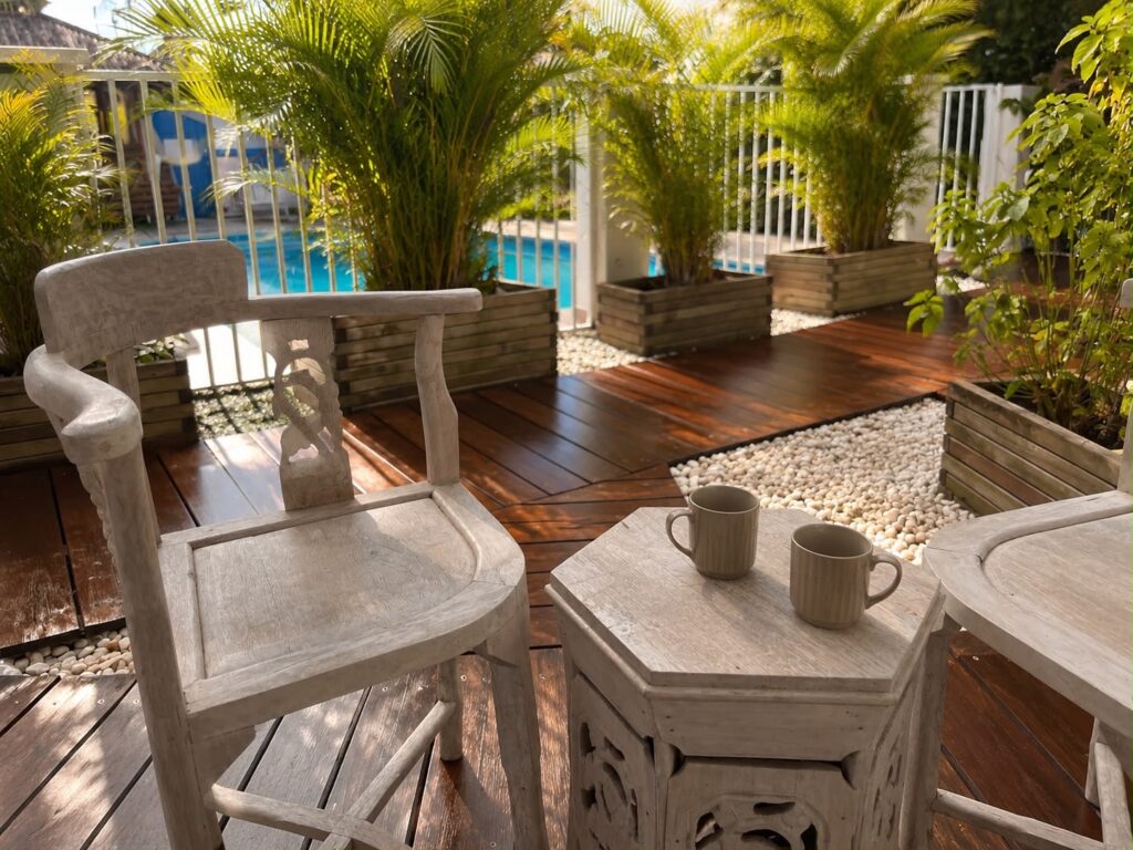 Terrasse privative en bois avec vue sur la piscine et les palmiers du gîte Bois de l'Encens, Les Bois d'Orée